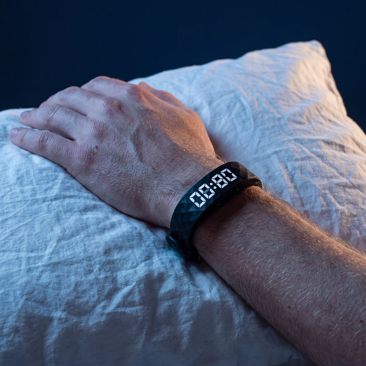 The WakeWave band on a sleeping wrist resting on a pillow